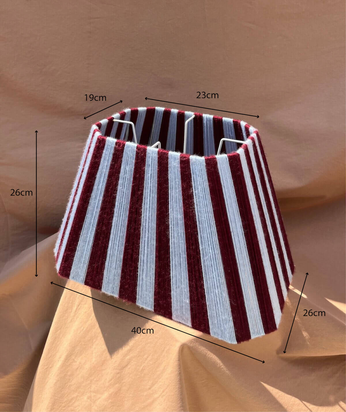 A Slice Shades yarn lampshade lampshade with vertical stripes in deep burgundy and light blue, displayed on draped tan fabric with dimensions