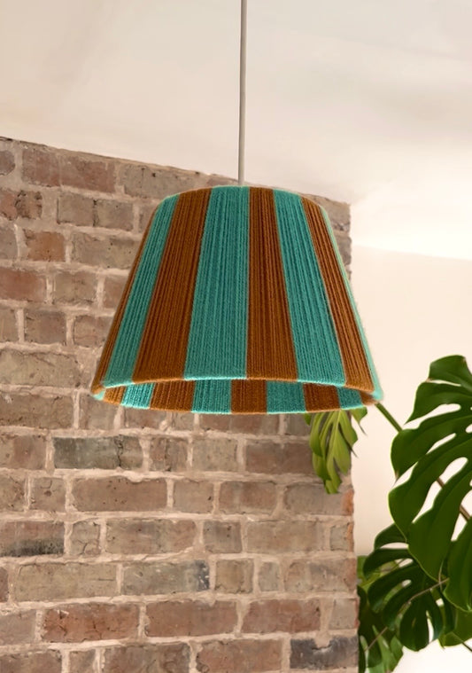 A pendant light with a Slice Shades yarn lampshade featuring alternating turquoise blue and rust-orange vertical stripes.