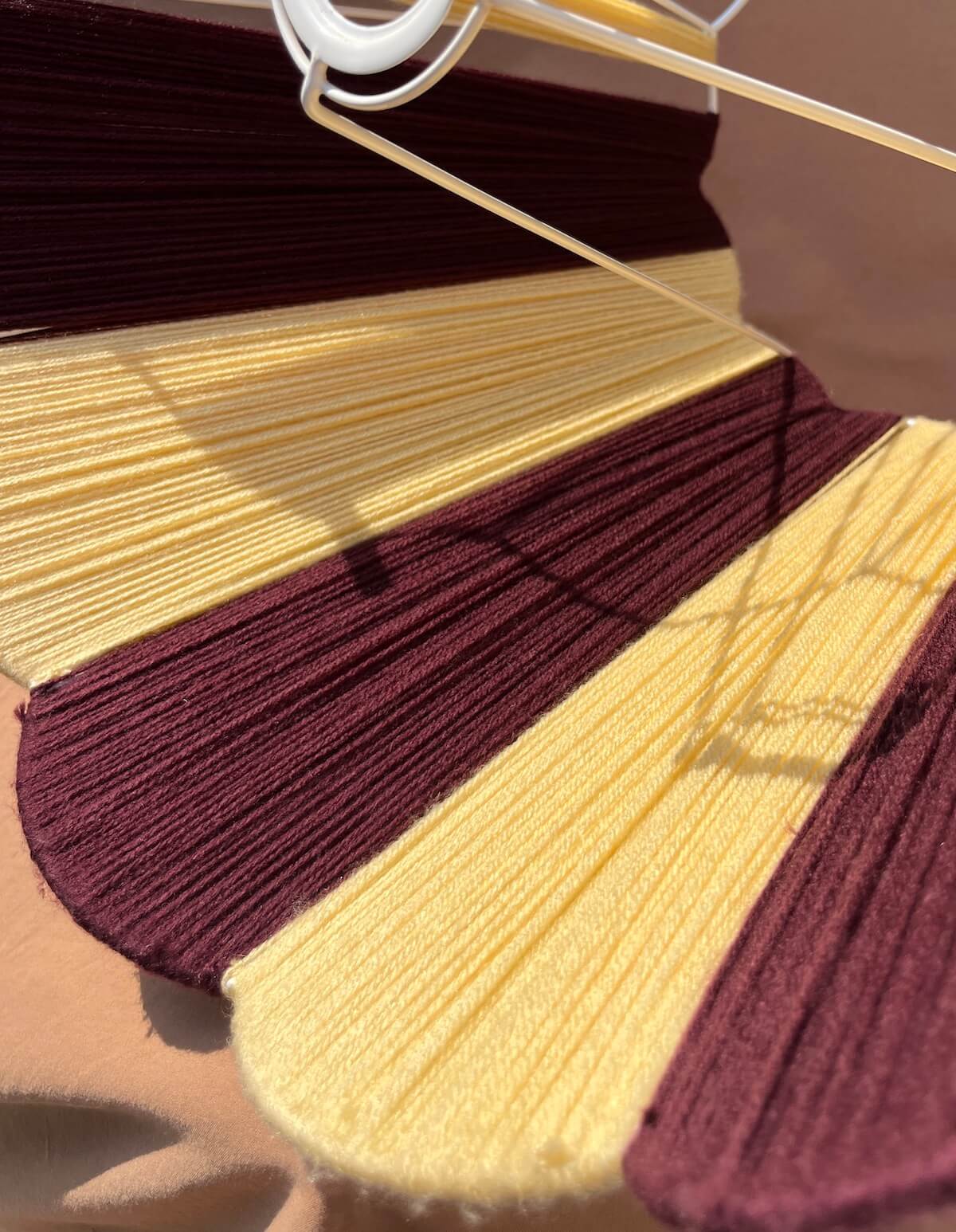A close-up of a Slice Shades Scallop Yarn lampshade in alternating dark burgundy and pale yellow, arranged in curved segments.