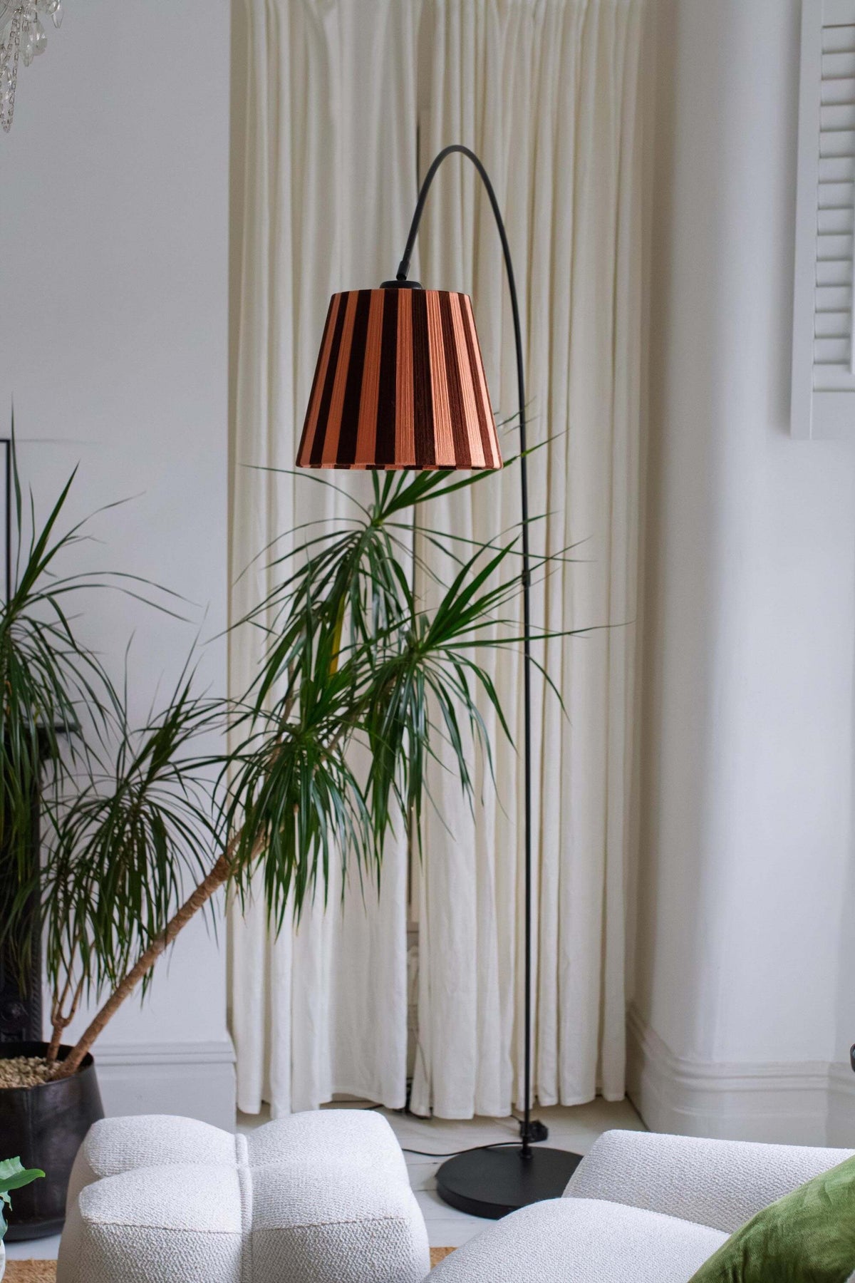 A black lamp stand with a slice shades handwoven yarn lampshade with vertical stripes in cocoa and plaster pink, hanging from a black cord in an indoor room setting.