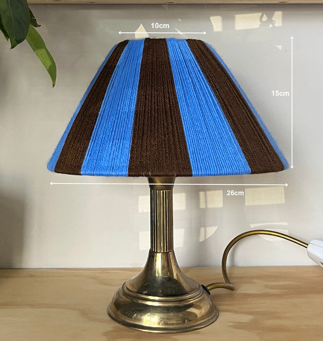 A table lamp with a Slice Shades blue and brown striped yarn shade and a metallic gold base, shown on a wooden surface with white dimension lines indicating measurements of 10cm, 15cm, and 26cm.