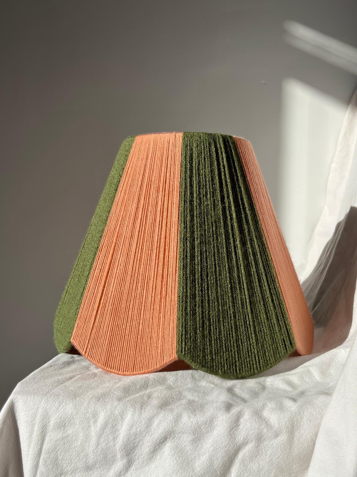 A slice shades handwoven striped scallop yarn lampshade in olive green and plaster pink with white background.