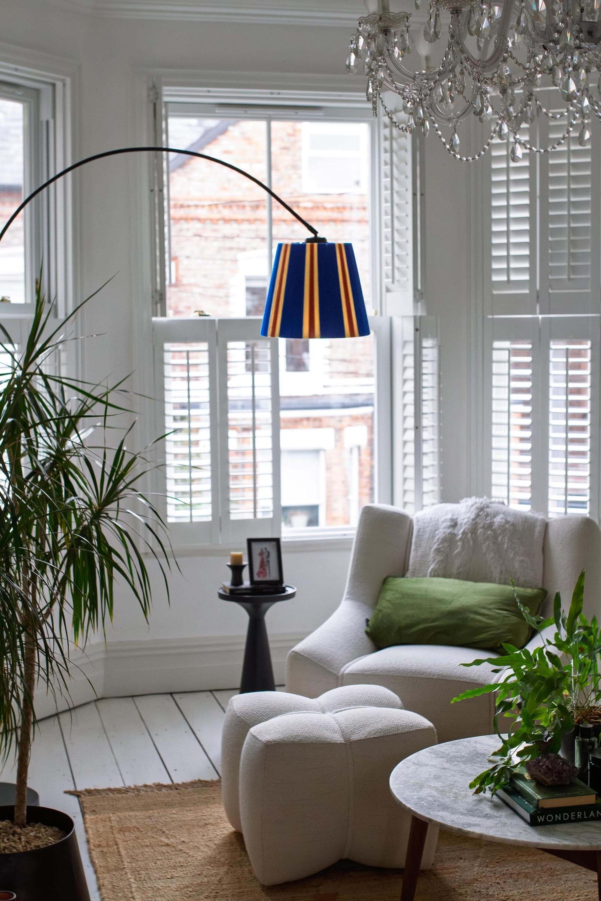 A modern black floor lamp with a slice shades majorelle blue striped yarn lampshade, styled in a room with a cream curtain and green plants.