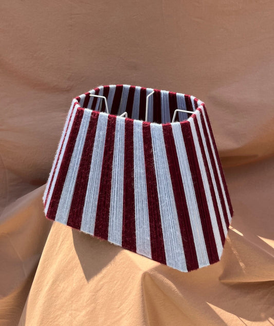 A Slice Shades yarn lampshade lampshade with vertical stripes in deep burgundy and light blue, displayed on draped tan fabric.