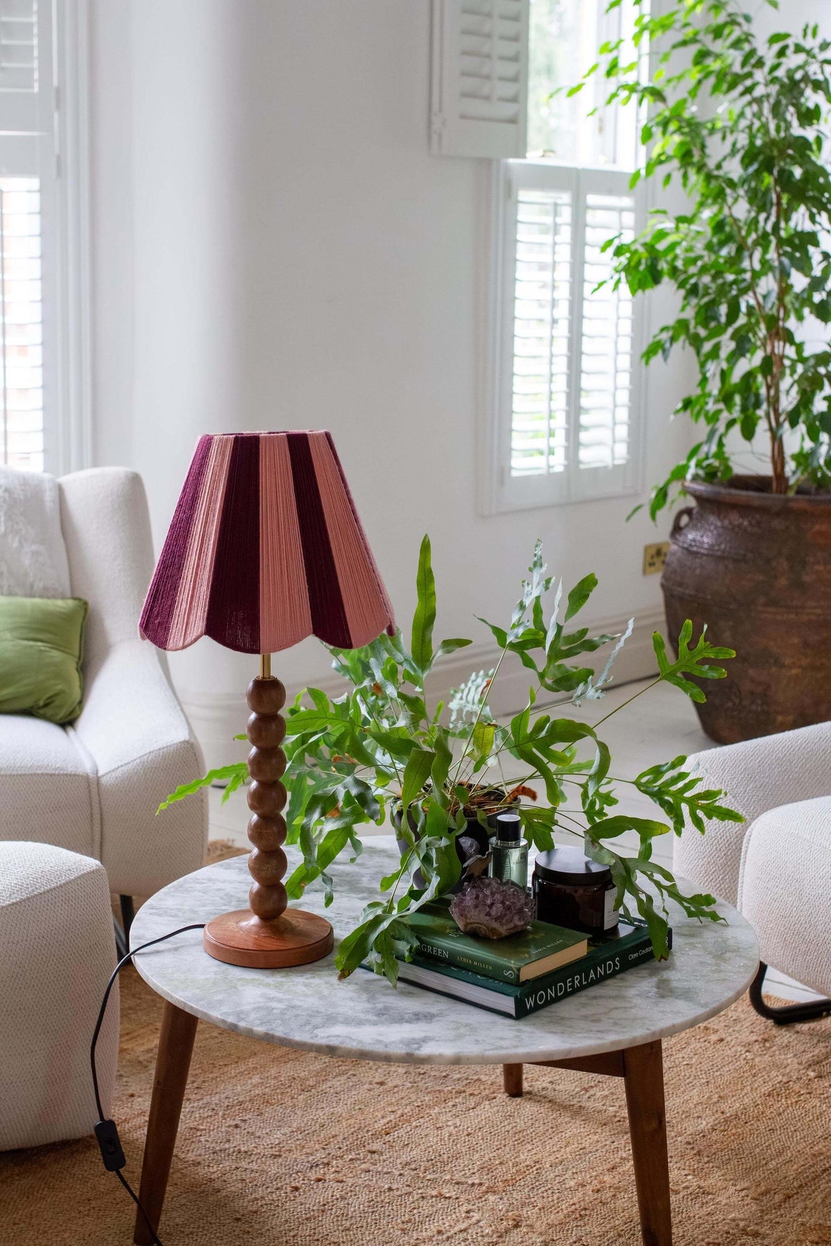 A mid-century modern table lamp with a slice shades handwoven yarn lampshade, set on a marble-top side table in a bright, modern living room.