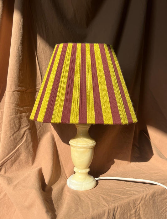 A handmade Slice Shades lampshade in stripes of chartreuse and mulberry yarn on a marble base.