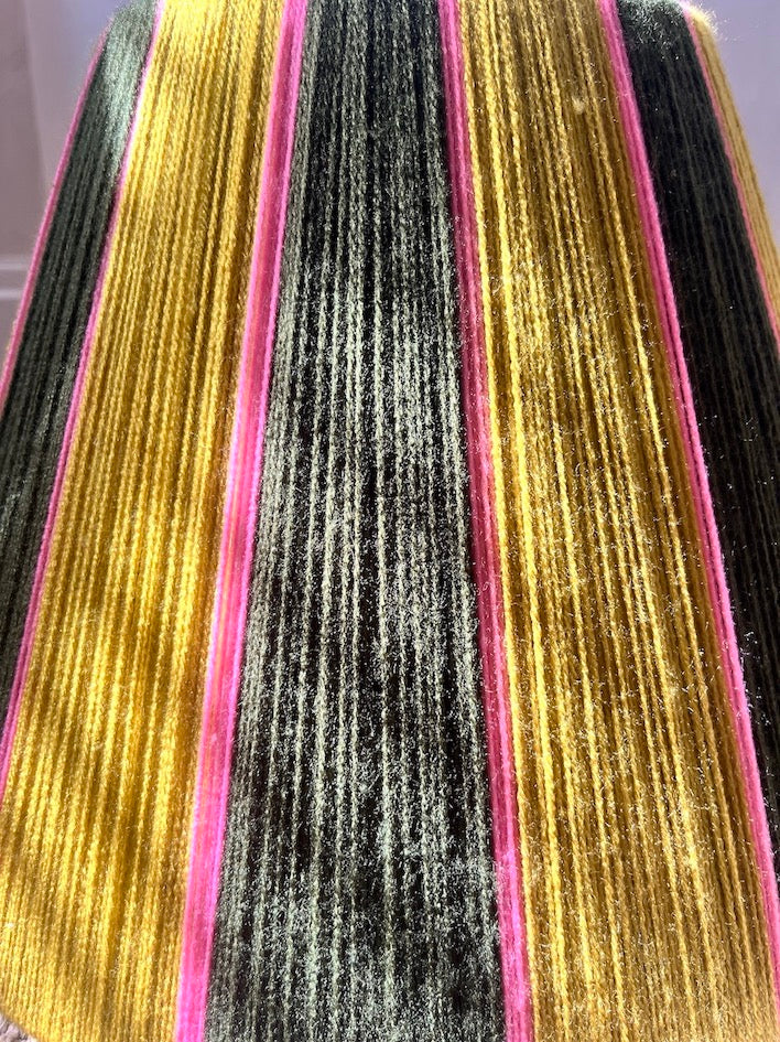 A close-up of a striped Slice Shades yarn lampshade with vertical bands of dark green and lime green stripes separated by bright pink borders.